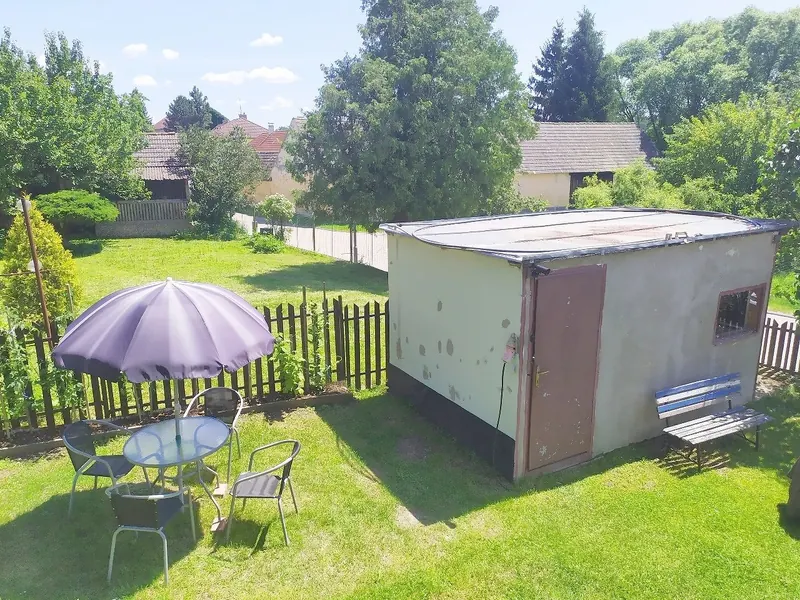 Zahrada penzionu s trávníkem, stolem a slunečníkem